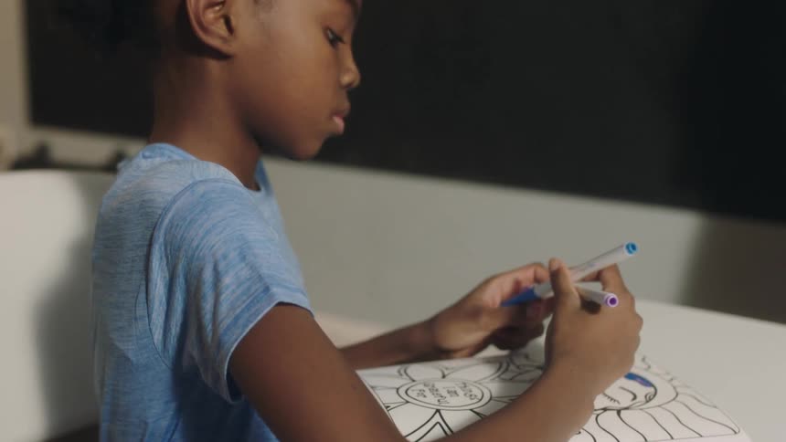 A girl uses markers to color in a coloring book