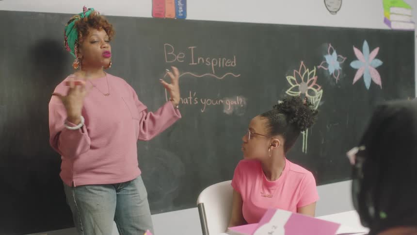 A teacher gestures with her hands while speaking to her students in a classroom