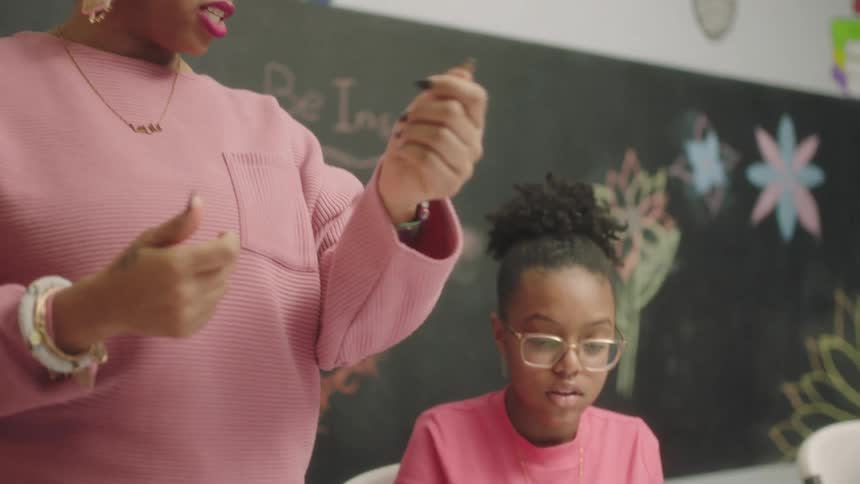 A teacher speaks to a student sitting at a table in classroom