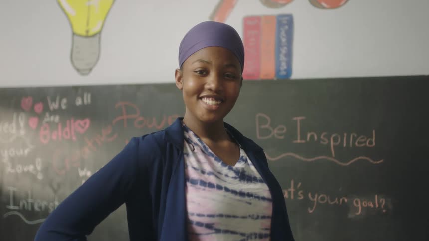 Girl poses smiling in front of blackboard with inspirational sayings on it