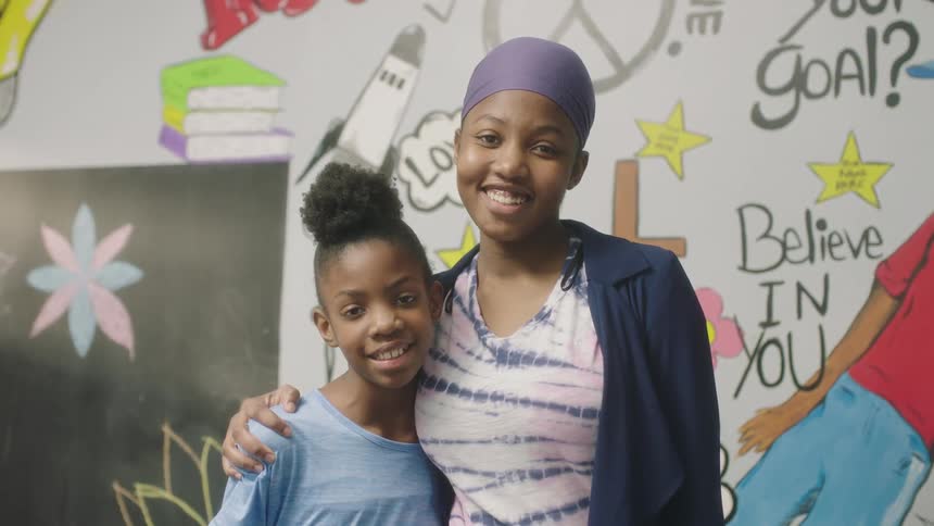 Students with purple headband white and blue top look at camera smiling in classroom at school