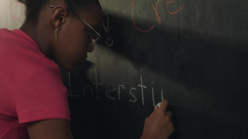 A girl misspells a word while writing on a blackboard with chalk