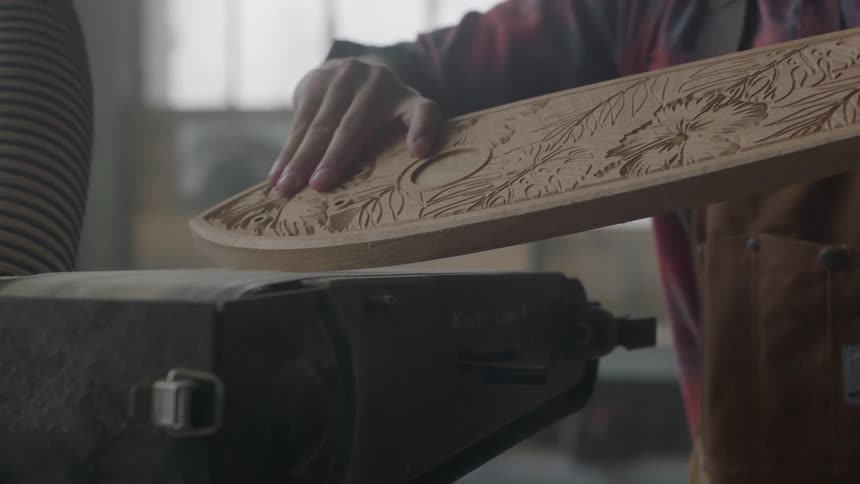 A man is shaving wood on a belt sander