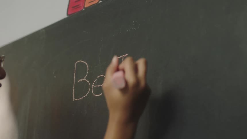 A young girl writes on a chalk board at school