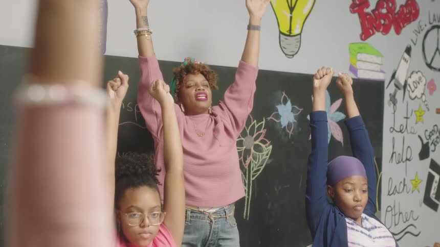 A teacher leads her students in stretching their arms over their heads