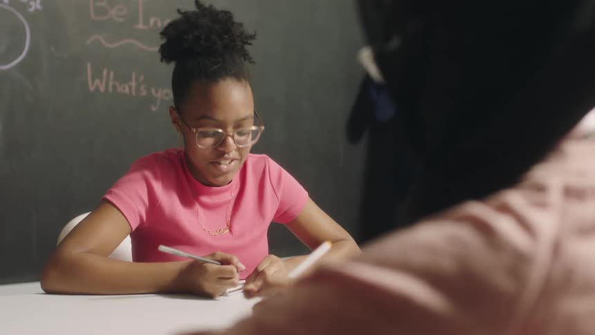 A pair of girls talk while during their schoolwork in a classroom during the day