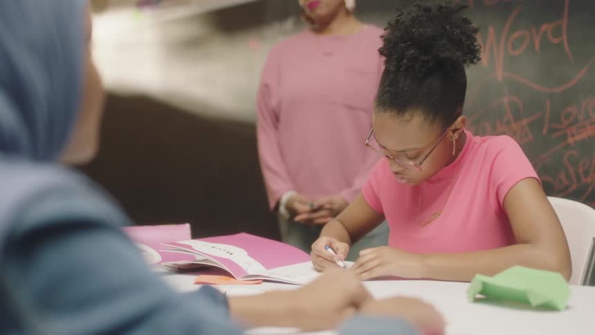 A teacher smiles while watching a pair of students work in a classroom