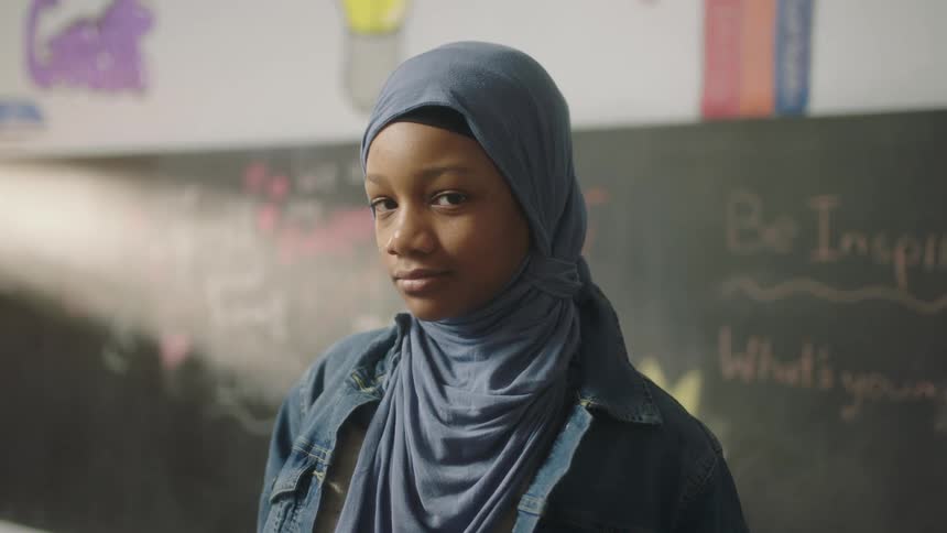 A girl stands in front of a chalk board at school