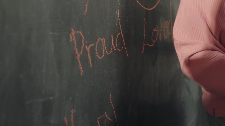 A woman writes on a blackboard using a piece of chalk