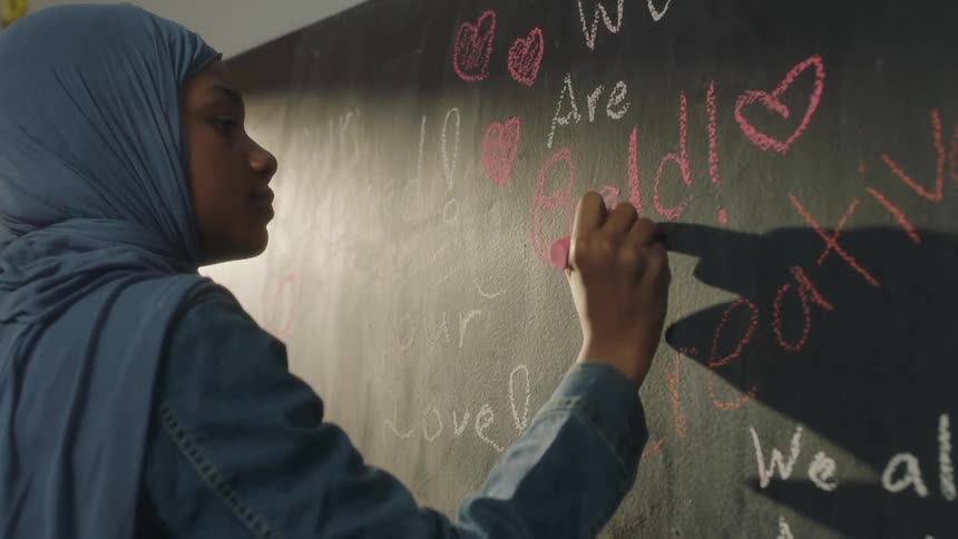 A student draws and writes on a chalkboard with pink chalk