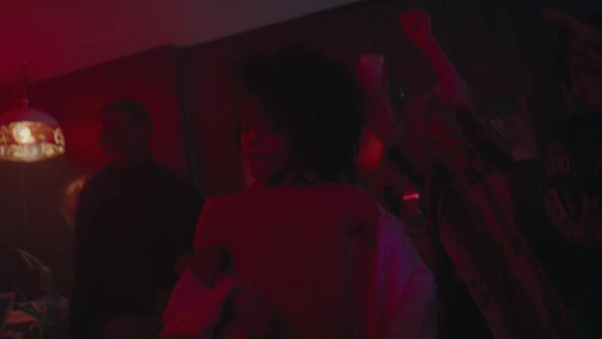 Party attenders cheer as woman dances in room lit by colored lighting