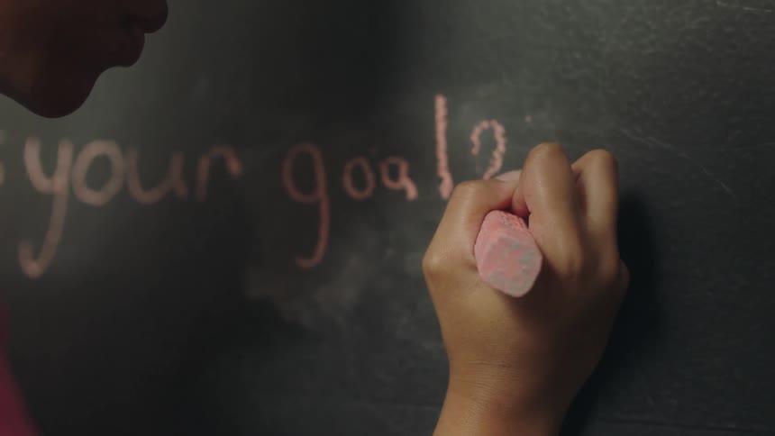A girl writes on a blackboard using a large piece of chalk
