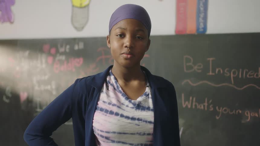 A teenager stands in front of a chalk board at school