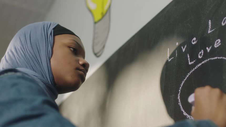 A young girl draws on a blackboard at school