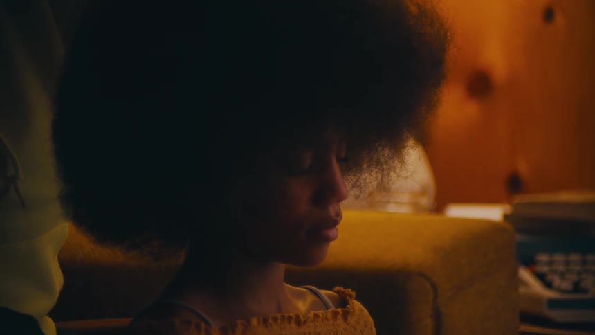 A teenage girl sits and reads at home as someone behind her pats her hair