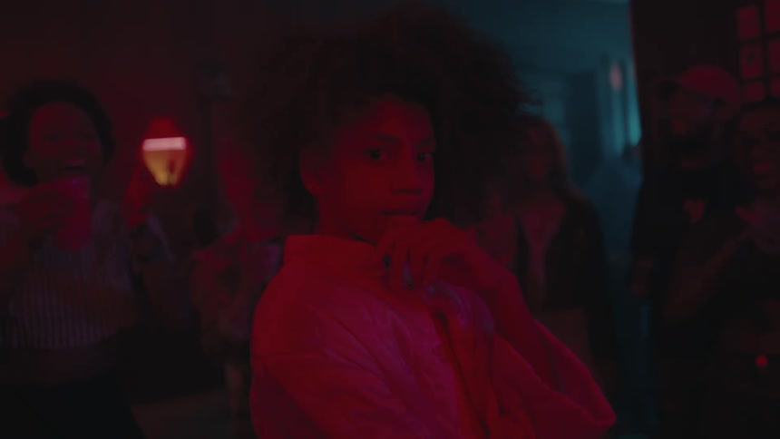 A woman stands in front of people clapping and dancing in a night club