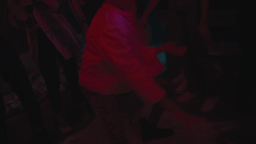 Person dances while a group of people stand nearby watching him in a dark room