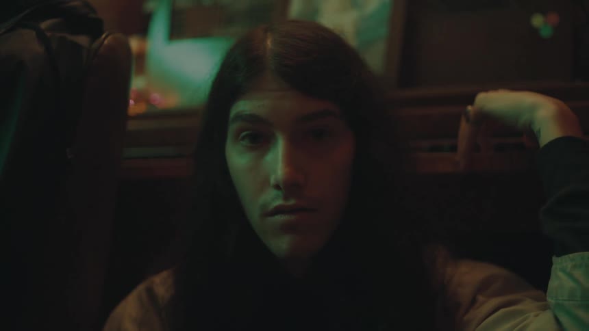 Man with long dark hair sits in front of a table that has a picture on it