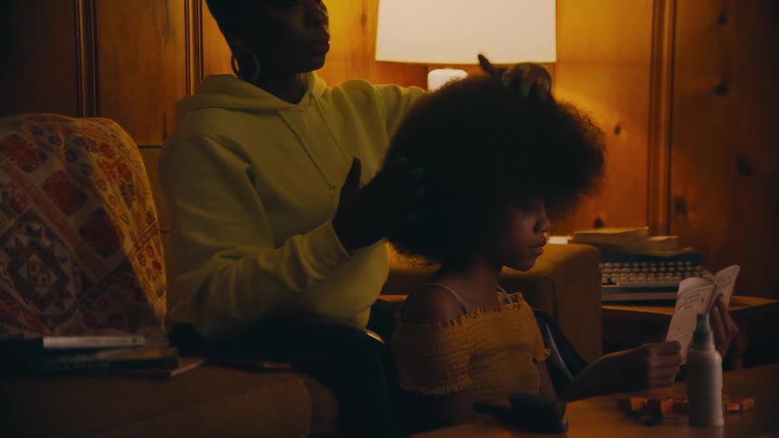 Woman styles daughters hair as daughter reads