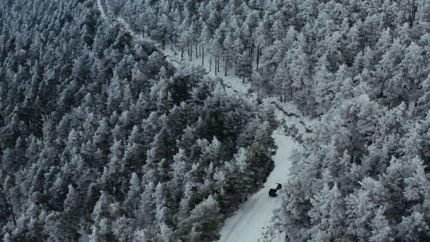 A sport utility vehicle drives down a snow covered road winding through a forest