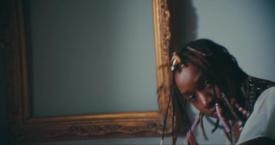 A young woman with braided hair dances while looking into the camera