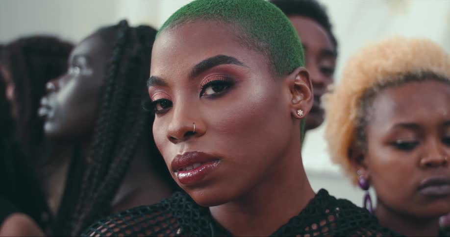 A woman standing with a group of women raises her gaze to look into the camera before looking away