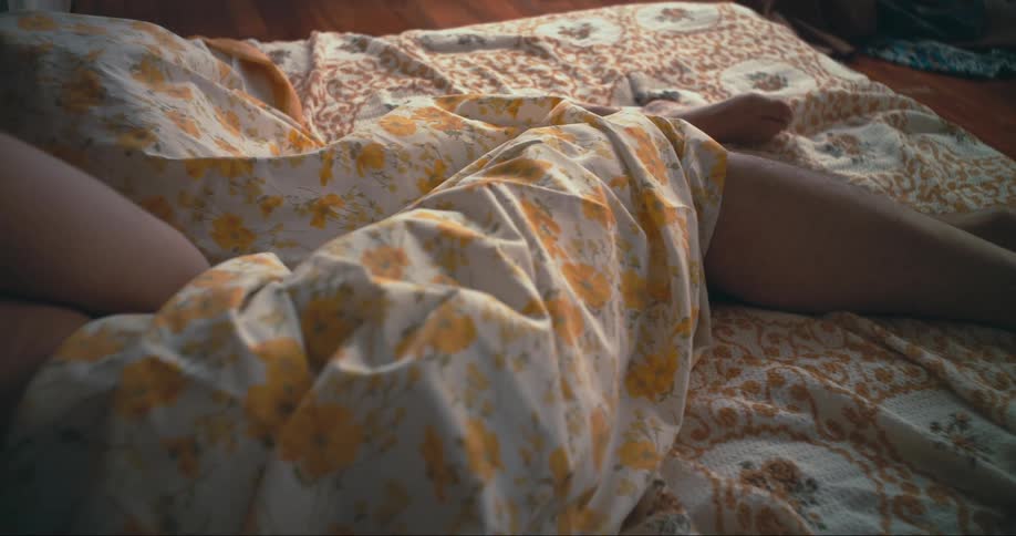 Couple lies on bed under floral sheet in room with wooden floor
