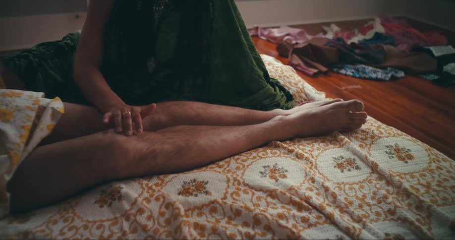 A woman caresses her partners legs while he lies in bed