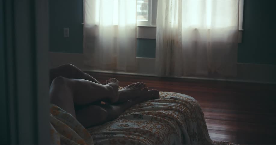 Man and woman lies on bed making out and touching each others legs in bedroom
