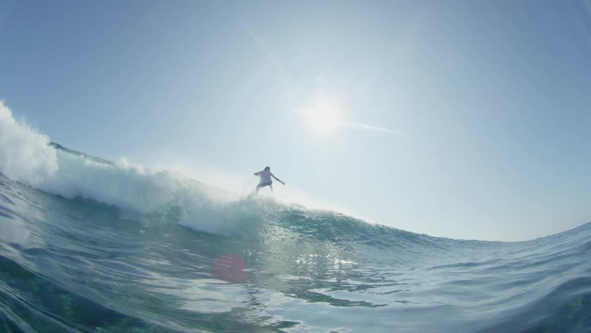 A young male on a surfboard glides across the edge of an ocean wave