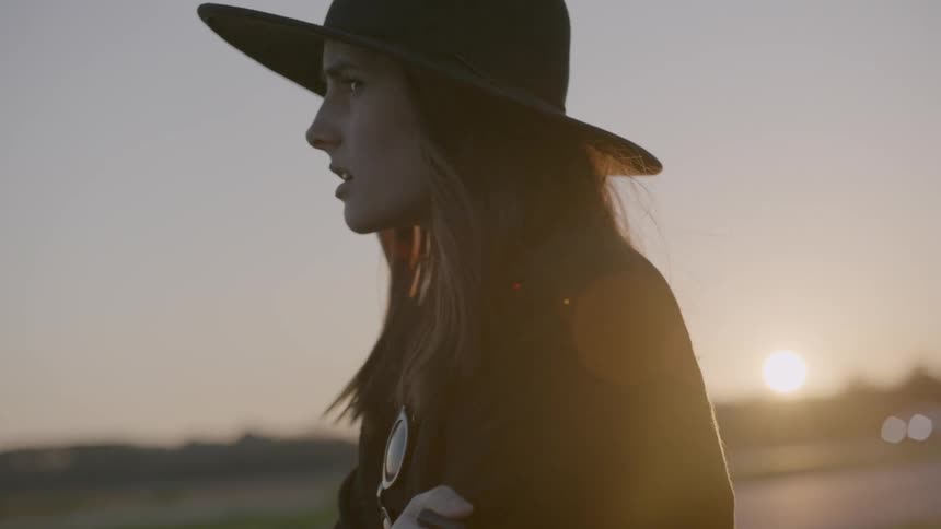 Woman wearing a hat next to a road at sunset