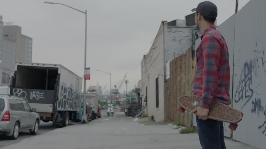 A man holding a skateboard stands on a city sidewalk