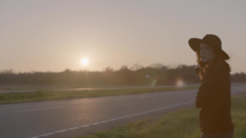 Woman in hat standing near a road at sunset