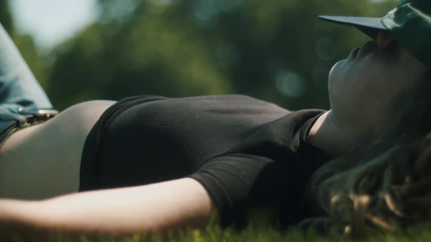 A woman lying in the grass with a cap over her eyes and her shirt pulled up to sunbathe