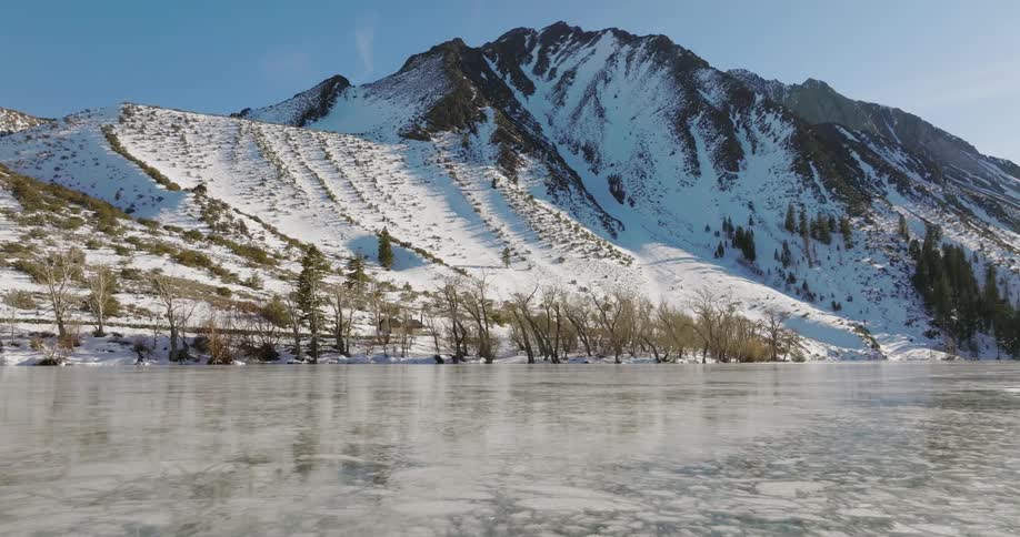 Ice covers a lake and there is a snow covered mountain ridge under a clear sky