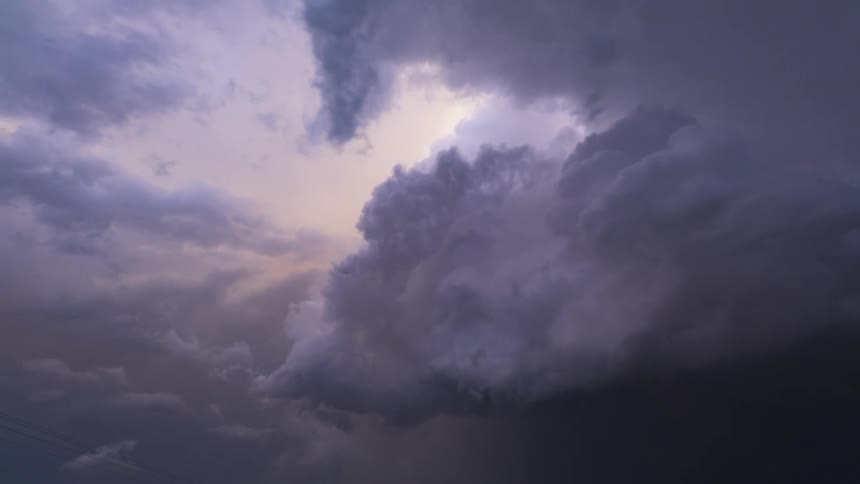 Storm clouds roll in and grow darker as lightning flashes behind them