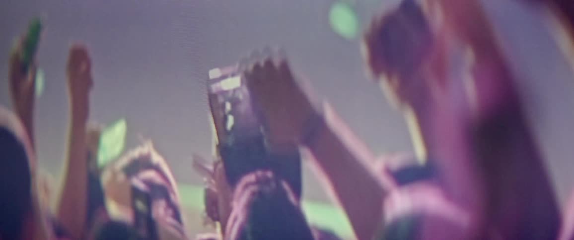 Crowd attending concert hold their arms and phones up as they jump up and down