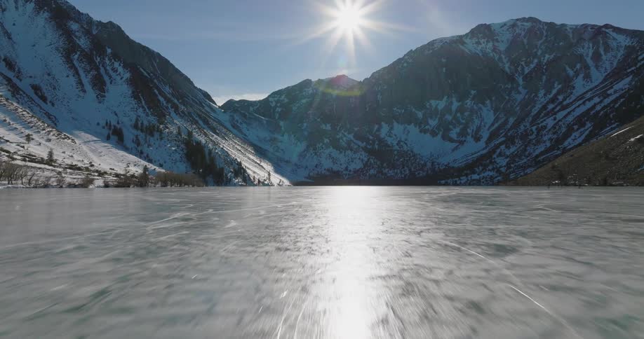 A thick layer of ice covers a lake below a mountain range