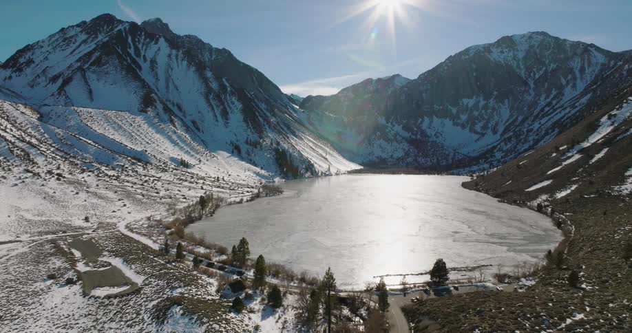 A layer of ice covers a lake at the base of a mountain range
