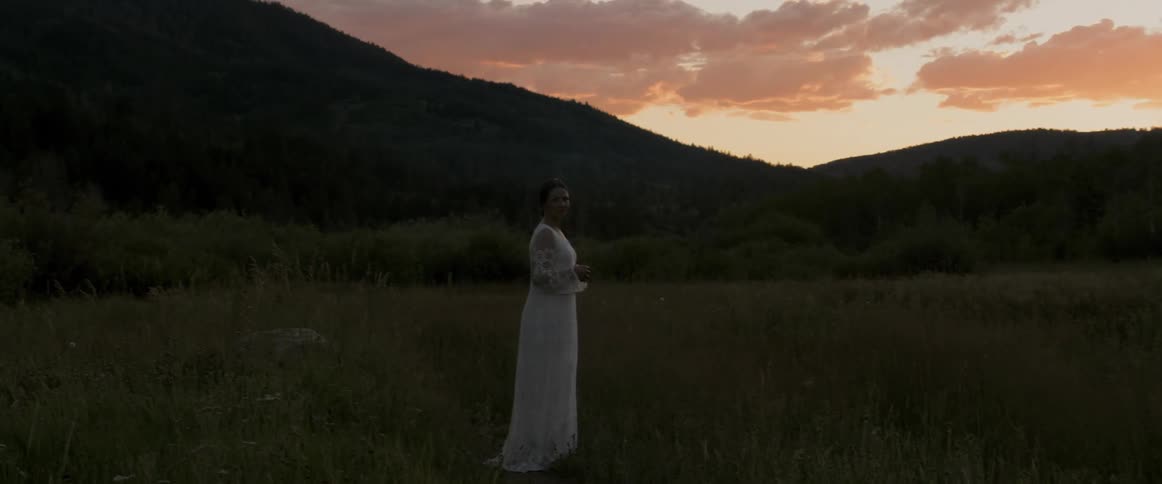 A woman is posing on the grass field in a white dress