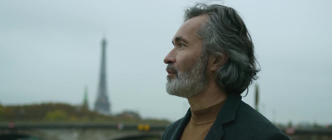 A man looks off in the distance while standing near a bridge downtown