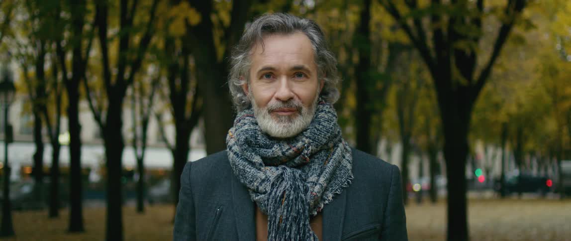 A man bundled in a coat and scarf poses in a park