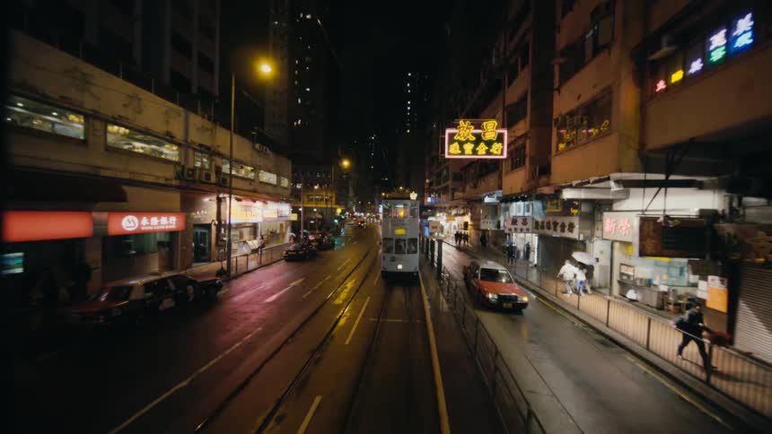A double decker trolley travels on tracks down the middle of a city street at night