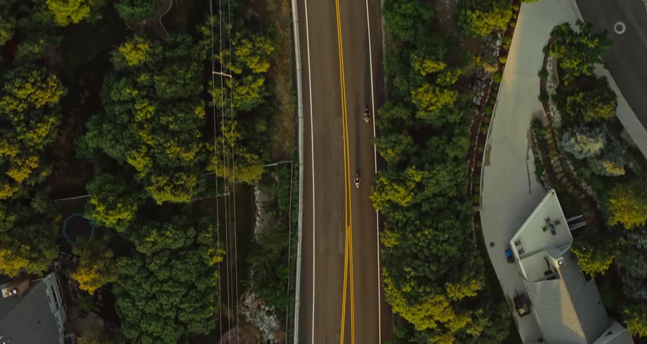 Aerial view of two motorcycles traveling on a road lined with trees and houses