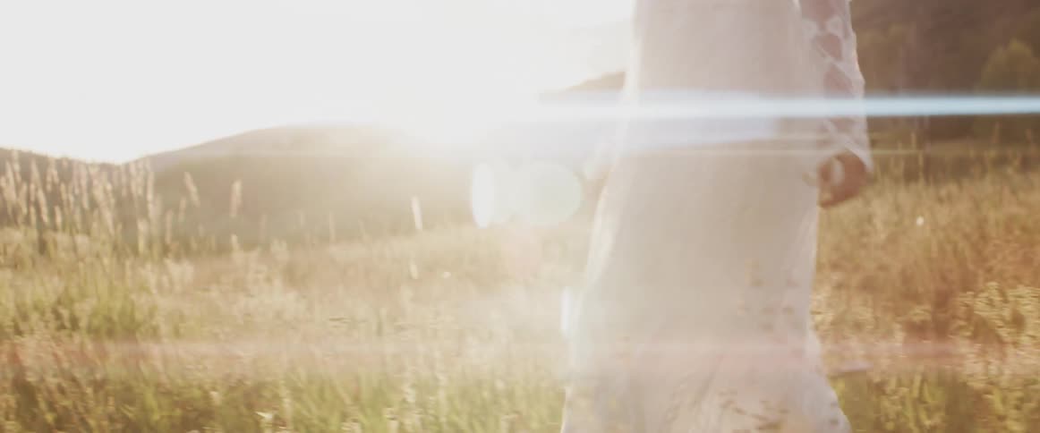A woman in a wedding gown walks through a grassland during the day