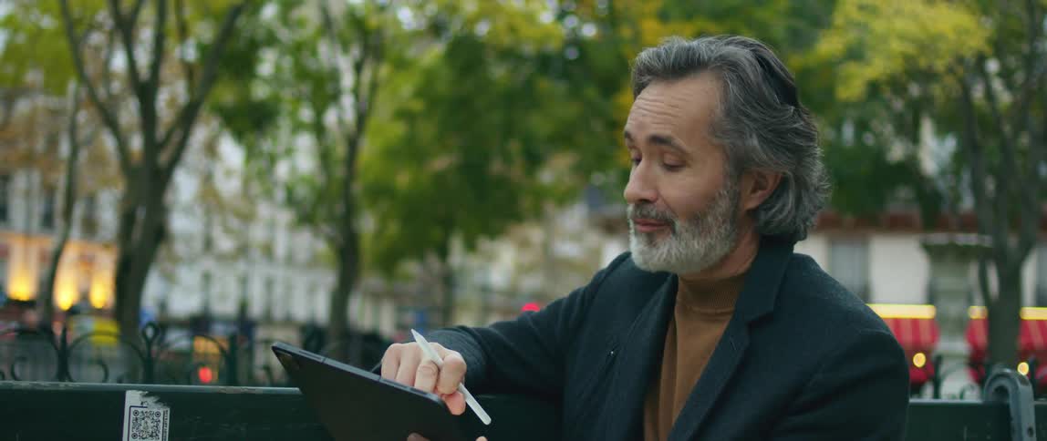 A man draws on his tablet while sitting in a city park