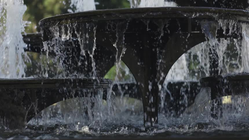 Fountains in a park are shooting water into the air and splashing as it drips down into the pool