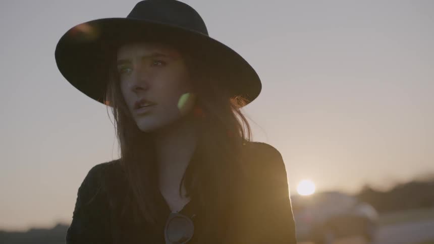 Woman wearing a hat next to a road at sunset