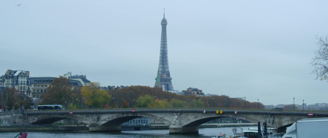 Traffic moves across a bridge and the eiffel tower is in the distance