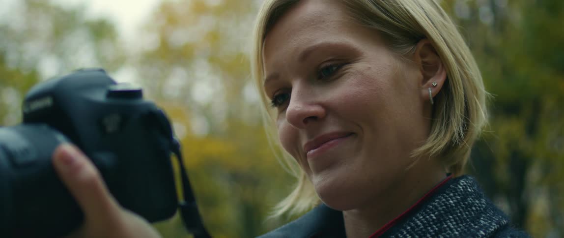 A woman with blond hair is smiling as she looks at the camera she is holding